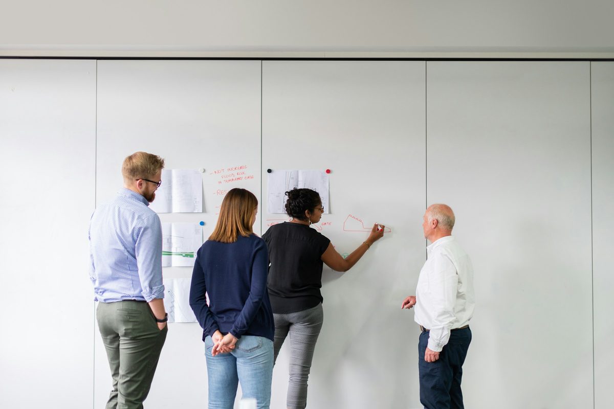 Four people standing at a whiteboard covered in notes, seen from behind